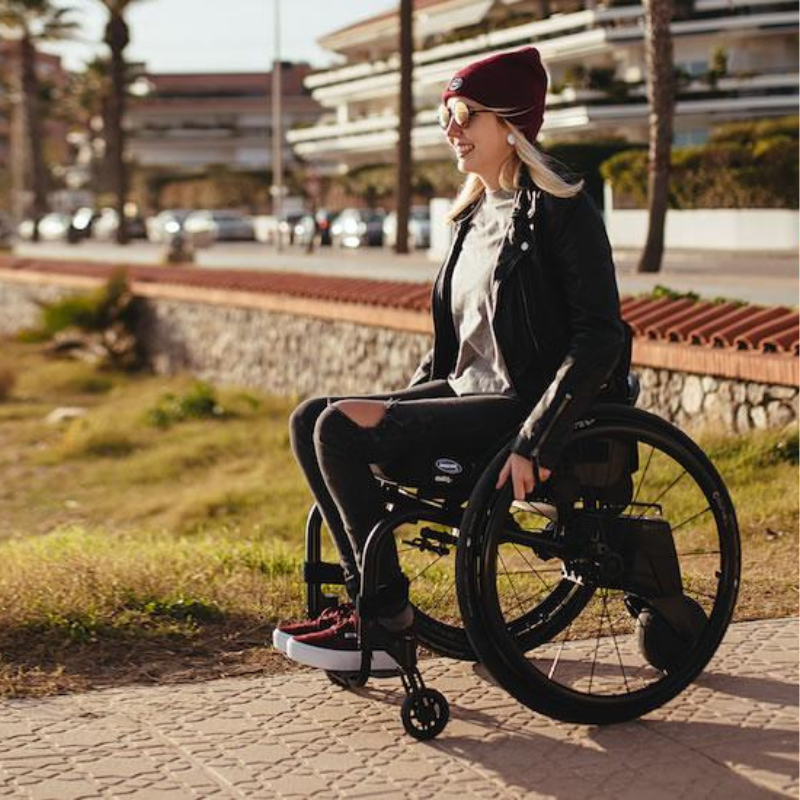 Mulher numa cadeira de rodas equipada com o Alber Smoov One, a deslocar-se ao ar livre num passeio.