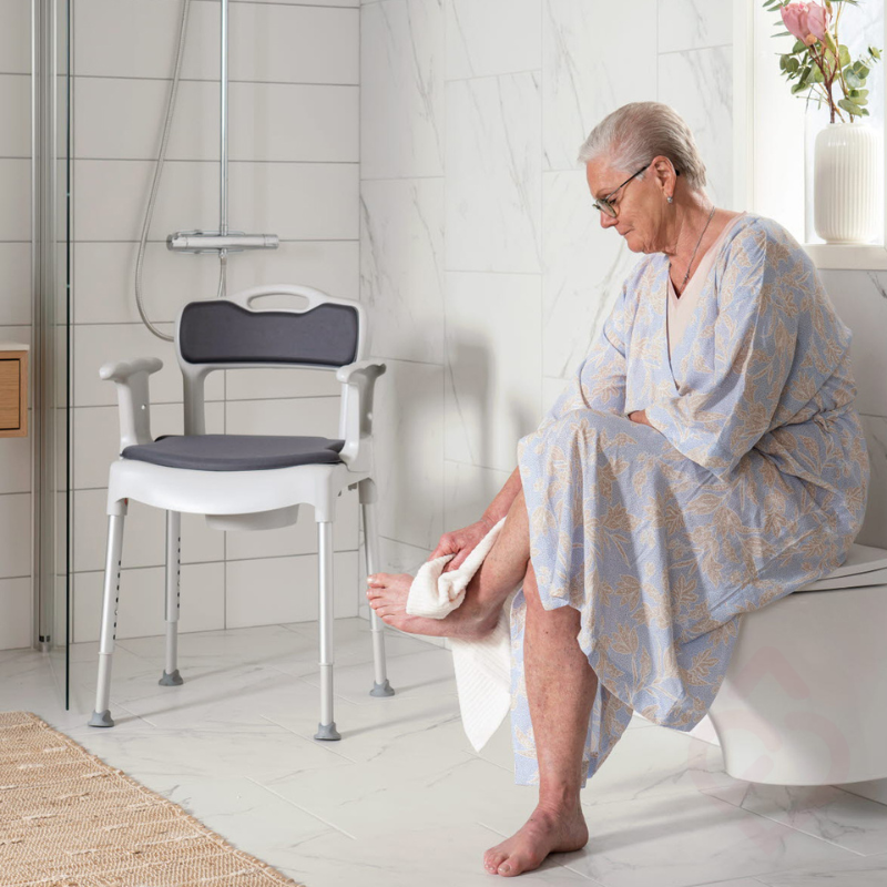 Cadeira sanitária e de duche regulável em altura, com braços de apoio, encosto e assento almofadado, colocada no duche