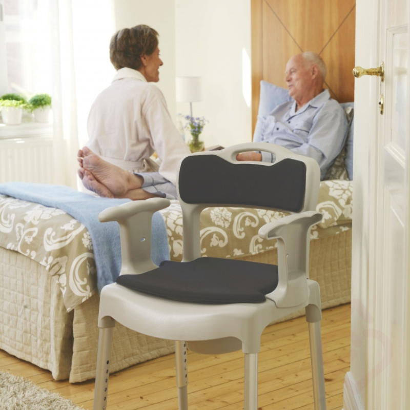 Cadeira sanitária e de duche regulável em altura, com braços de apoio, encosto e assento almofadado. colocada no quarto