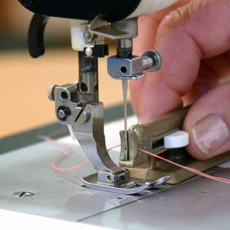 Enfia-agulhas em utilização numa máquina de costura, facilitando a passagem da linha pela agulha com maior rapidez e precisão.