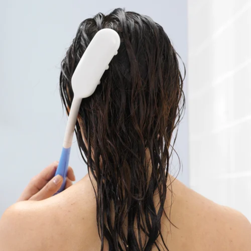 Pessoa a utilizar a escova de cabo longo no cabelo molhado, facilitando a lavagem e massagem do couro cabeludo sem necessidade de elevar tanto os braços.