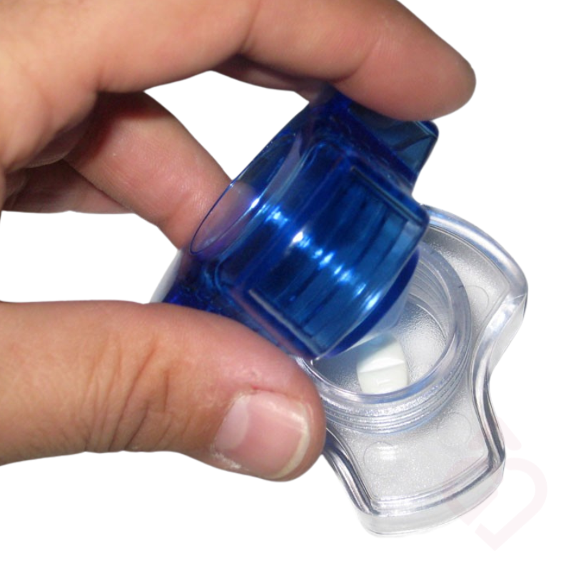 Mão a colocar um comprimido no triturador, com a tampa azul aberta.