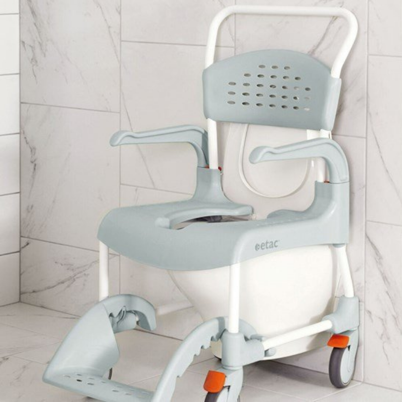 Cadeira de duche e WC com rodas posicionada junto à sanita para facilitar a utilização e as transferências